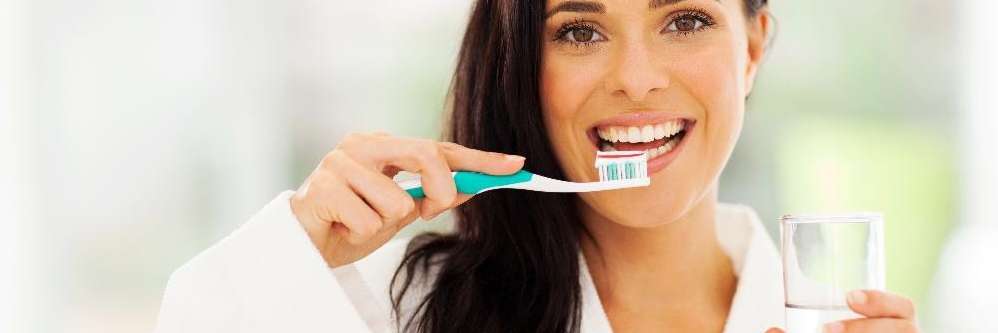 woman brushing teeth while holding a glass of water